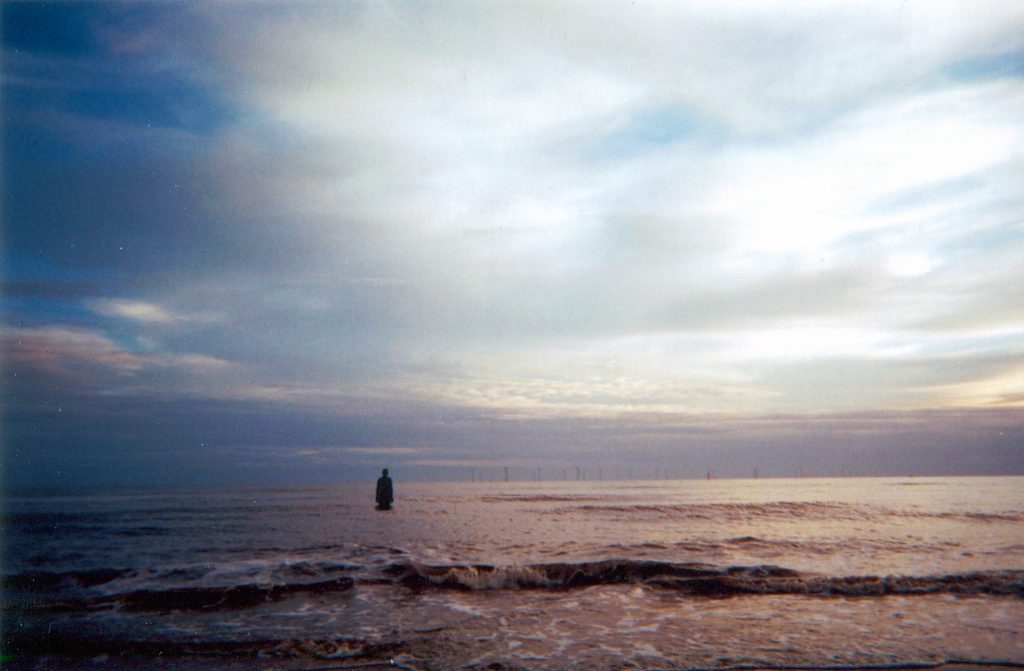 Photo of the sea, with clouds above and wind turbines in the distance
